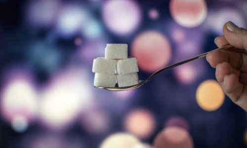 Sugar cubes on teaspoon in order to symbolize unhealthy fat, sugar and salt intake in our diet on a bokeh background.
